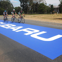 Autocollant rectangulaire géant apposé sur l'asphalte où roulent des cyclistes de compétition