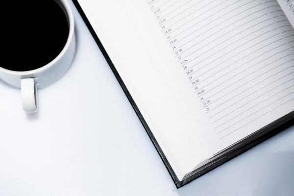 Agenda et café posés sur une table blanche