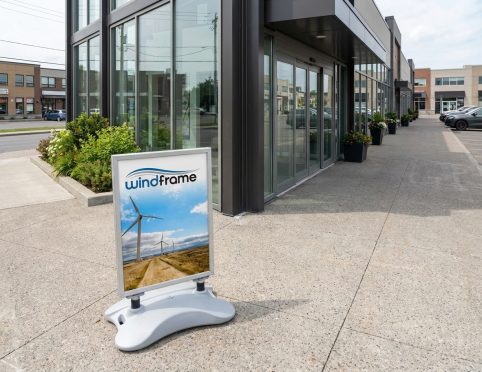 Porte-affiche Windframe installé sur le trottoir devant un commerce, affichant une image d'éoliennes sur un chemin de terre